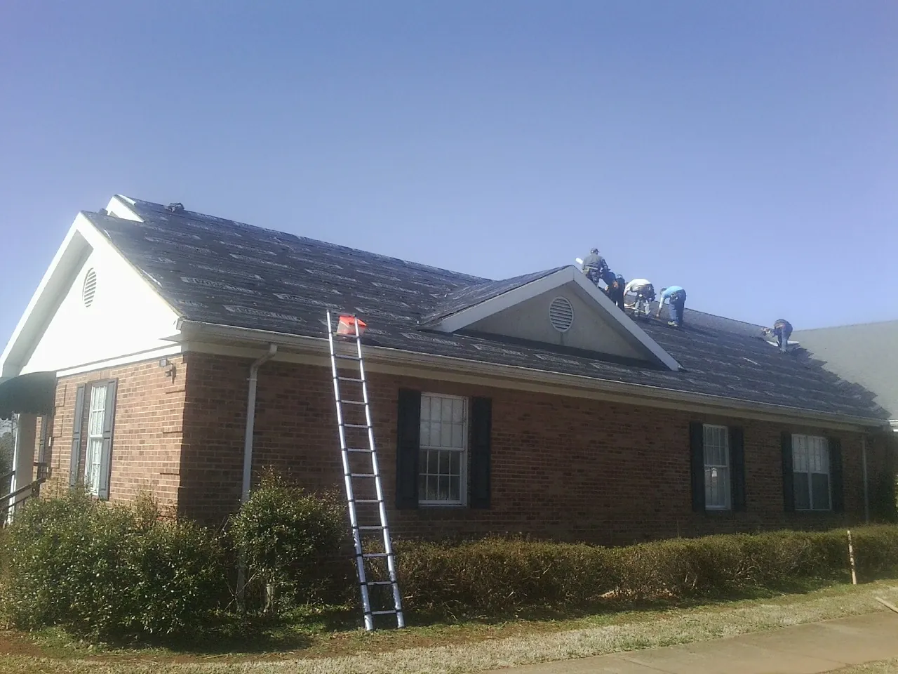 Crew tearing shingles off a brick ranch roof with a ladder set — Emergency Roof Repair work by our crew in Charles City