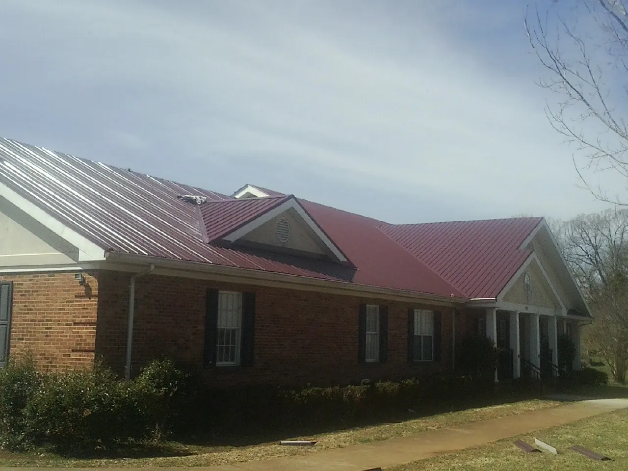 Red metal roof with gabled entries on a long brick building, from a Hail Damage Roof Repair job in Charles City