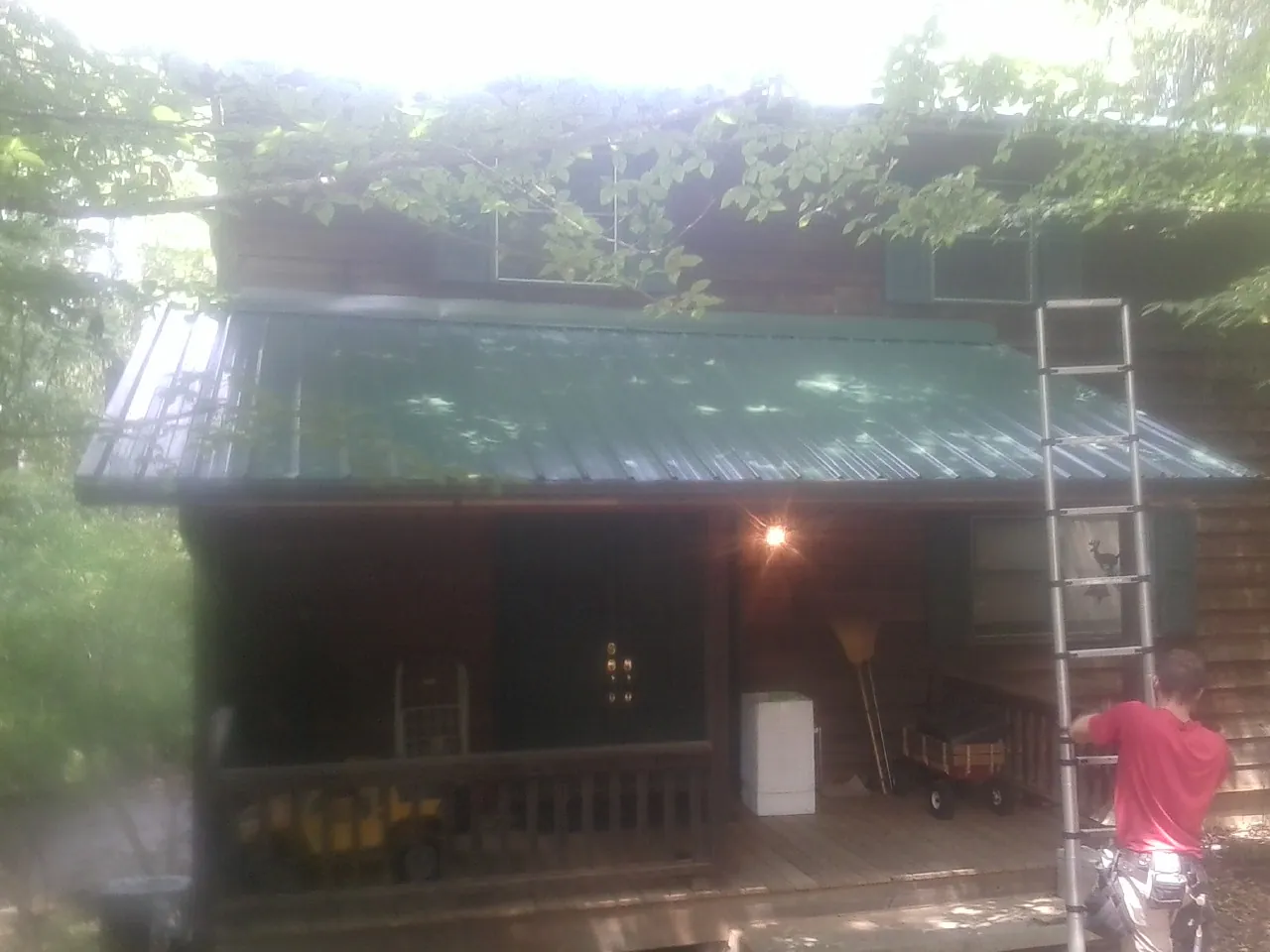 Worker on a ladder at the green porch roof of a wooded cabin in Charles City