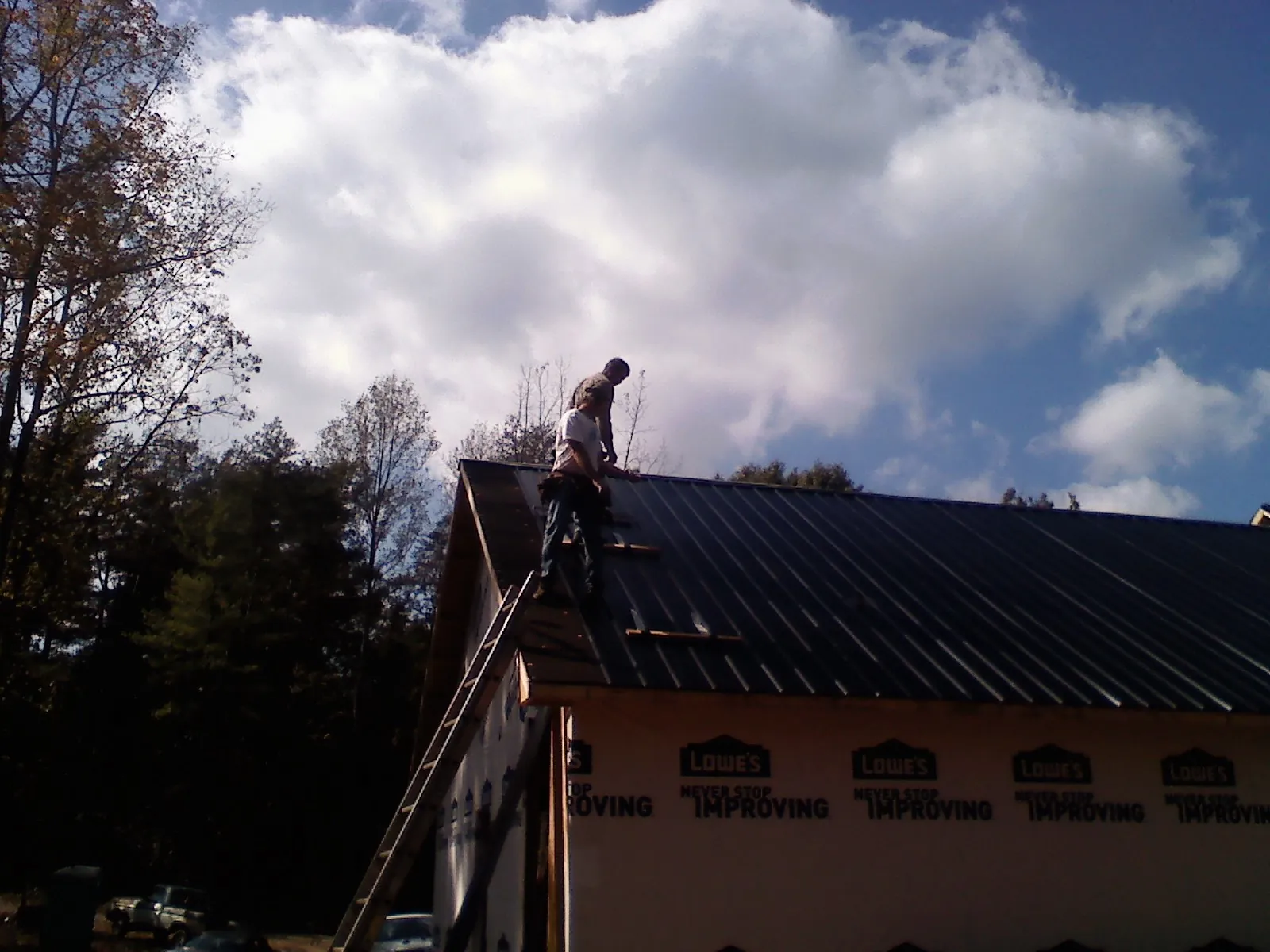 Roofer fastening dark metal panels high against a cloudy sky, from a Roof Inspection job in Charles City