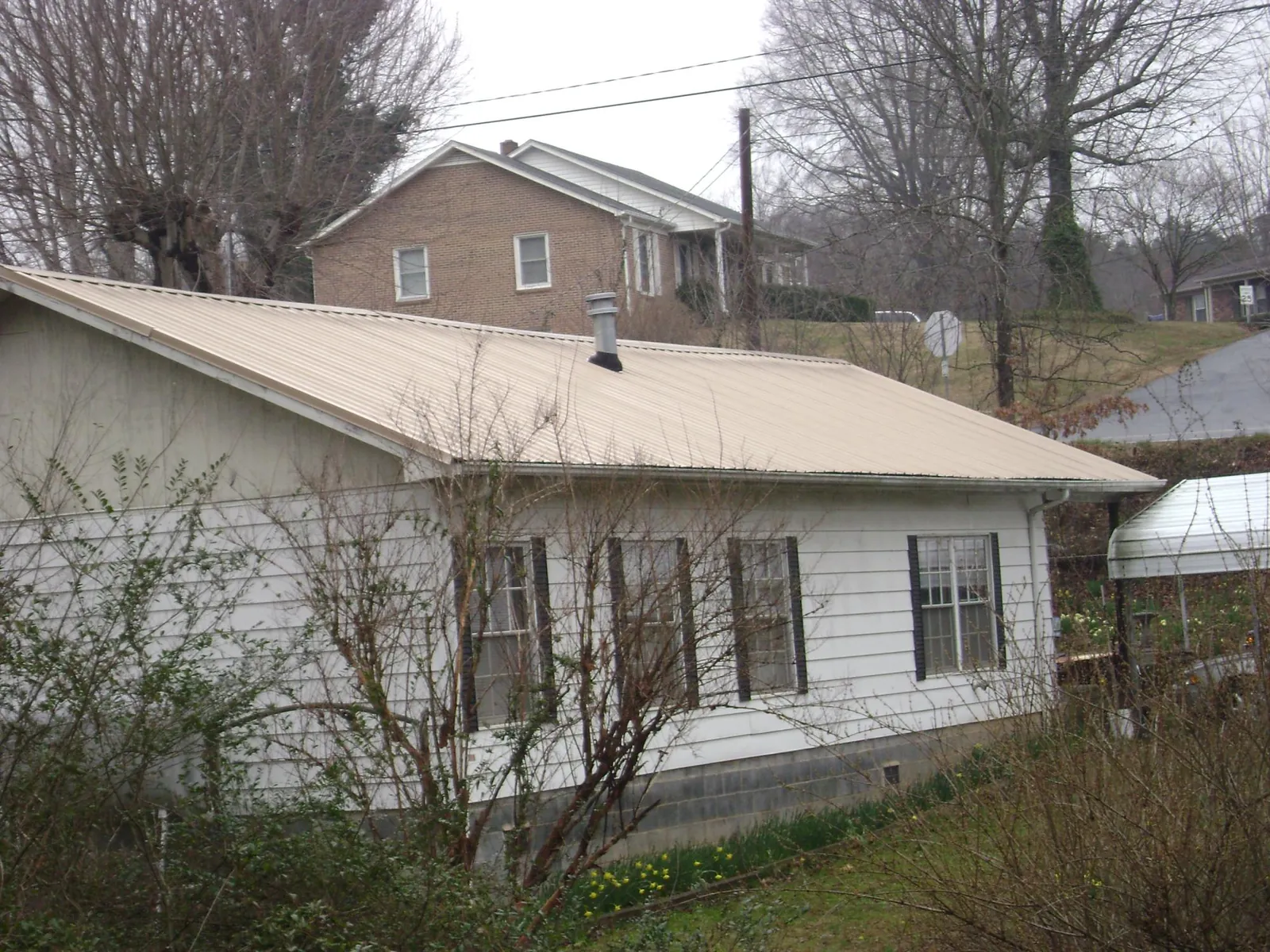 Tan metal roof on a white sided house set into a hillside — Commercial Roofing by Roofing Brothers in Charles City